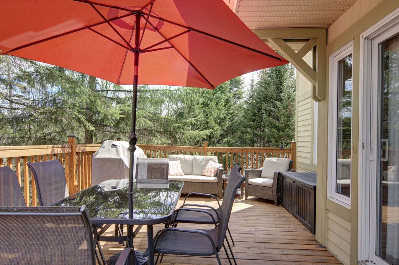 Une terrasse dotée de mobilier d’extérieur, d’une table en verre et d’un parasol rouge.