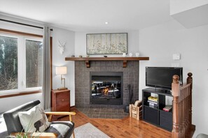 A living room with a fireplace, a television, and a bookshelf. - 4 Bedroom Family Townhome on La Bete Golf (Mont-Tremblant)