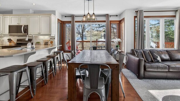 A modern kitchen with a central island, bar stools, a dining table, and a leather sofa.