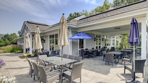 An outdoor patio with tables and chairs, covered by umbrellas, and a building in the background.