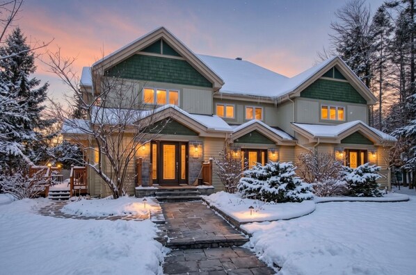 A two-story house with a snow-covered roof and a stone pathway leading to the entrance.