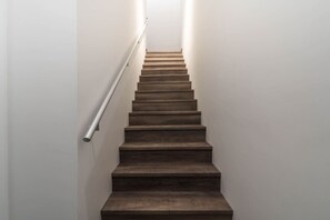 A staircase with wooden steps and a metal handrail, leading to a landing with a light source above. - The Timber Den with Indoor Hot Tub (Revelstoke)
