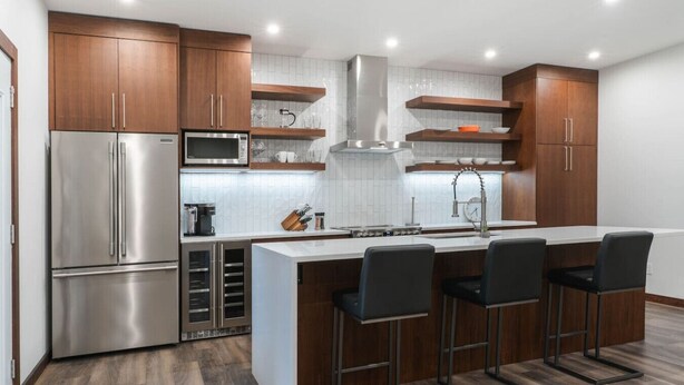 Een moderne keuken met roestvrijstalen apparatuur, houten kasten, een centraal kookeiland met barstoelen en een betegelde spatwand.