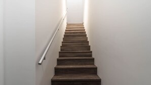 Een trap met houten treden en een metalen leuning, die uitkomt op een plateau met een lichtbron erboven.