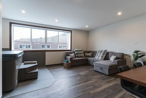 A modern living room with a large window, a sofa set, a small table, and a hot tub. - The Powder Den with Indoor Hot Tub (Revelstoke)