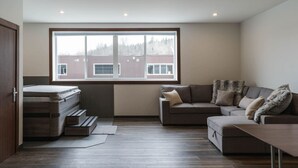 A modern living room with a large window, a sofa, a coffee table, and a bed with a mattress. - The Alpine Den with Indoor Hot Tub (Revelstoke)