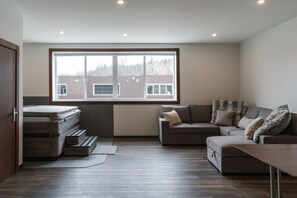 Ein modernes Wohnzimmer mit einem großen Fenster, einem Sofa, einem Couchtisch und einem Bett mit einer Matratze.