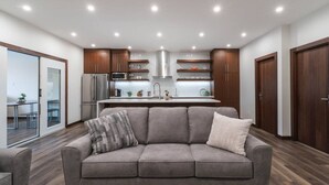 A modern kitchen with a grey sofa, wooden cabinets, and a dining area with a glass door. - The Alpine Den with Indoor Hot Tub (Revelstoke)