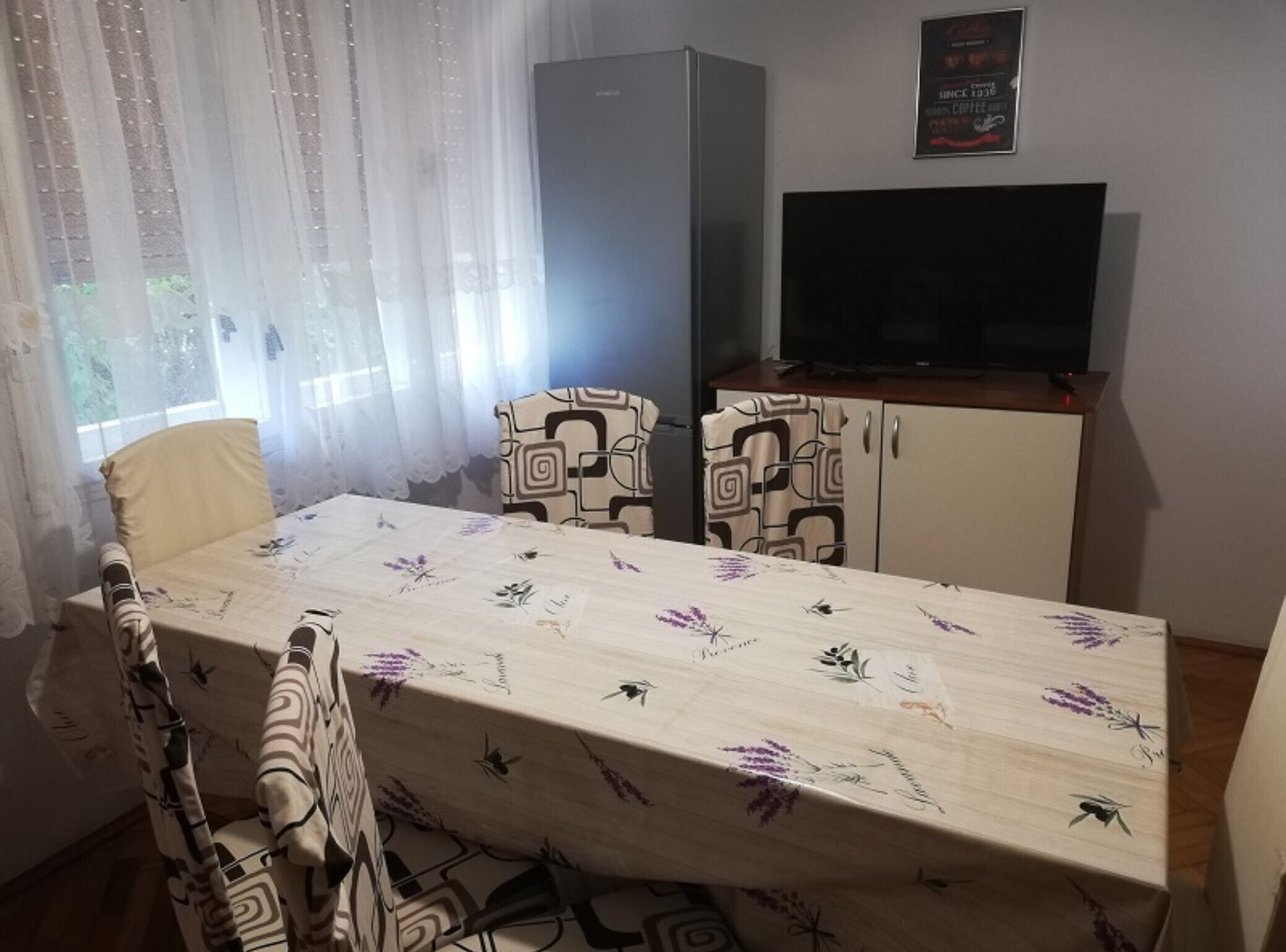 A dining area with a table, chairs, a refrigerator, and a television.