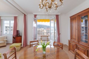 Una habitación con una mesa de comedor, sillas, una araña, un sofá, un mueble para TV y vistas a un balcón con toldo amarillo.