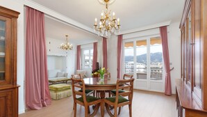 Ein Essbereich mit einem runden Tisch, Stühlen, einer Chandelierleuchtre und Blick durch große Fenster.