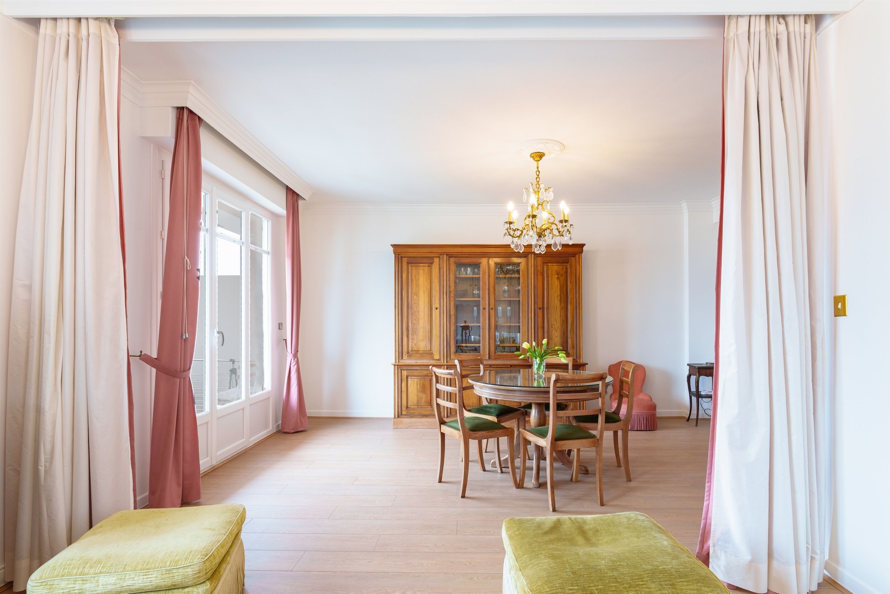 Un coin repas comprenant une table ronde, des chaises, un lustre et des meubles de rangement en bois.
