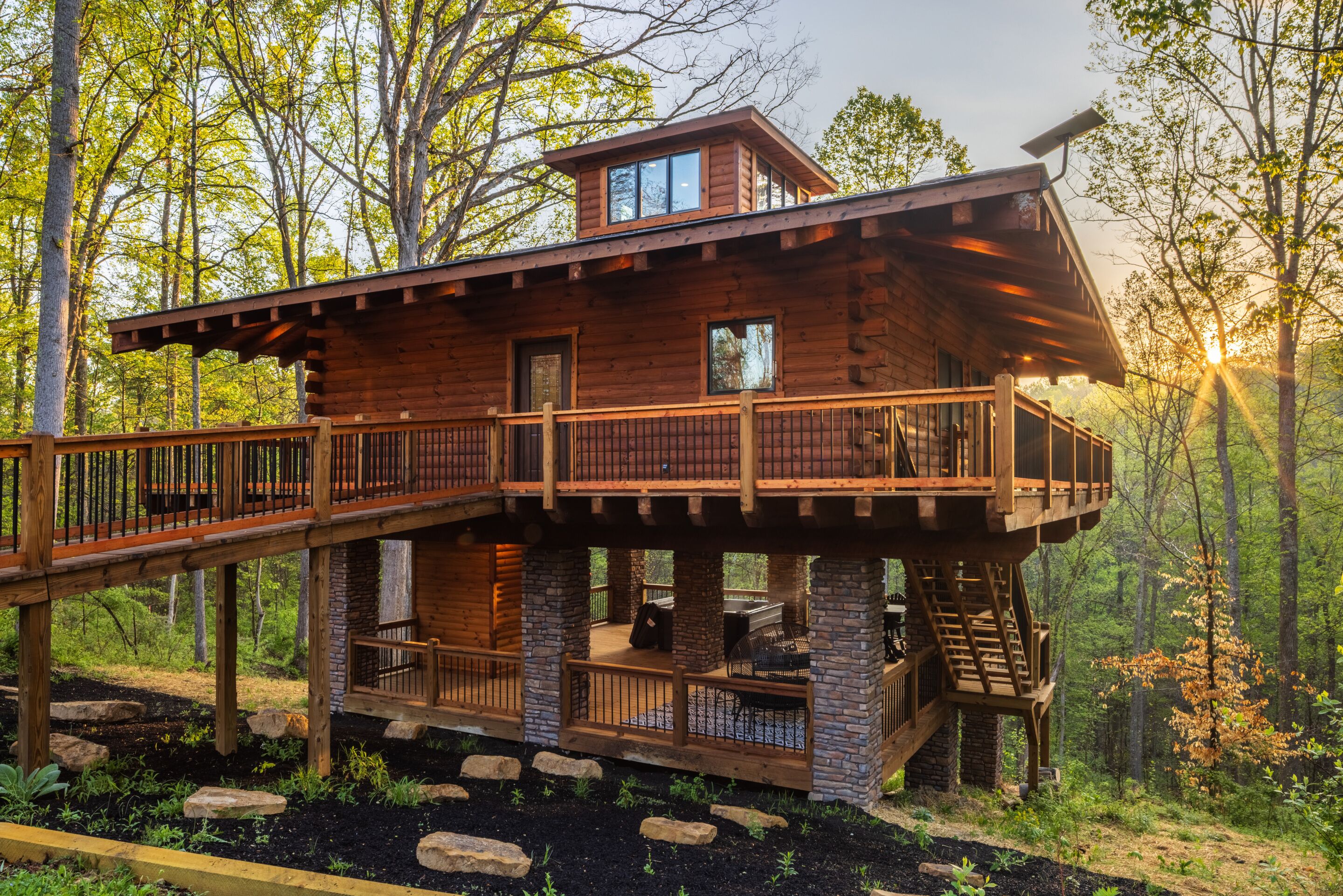 A cabin with a multi-level deck, stone pillars, and a wooden exterior.