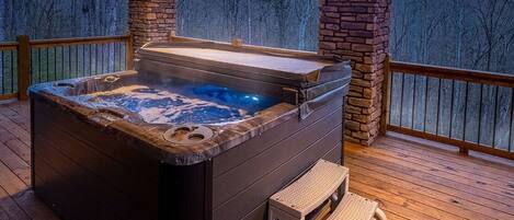 Un jacuzzi en una terraza de madera con un muro de piedra y vistas a árboles.