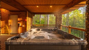 Ein Whirlpool in einer Blockhütte mit einer Holzdiele und Blick auf einen Wald.