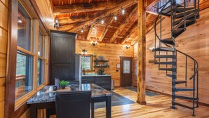 Een houten cabin met een keuken, eethoek en een wenteltrap.