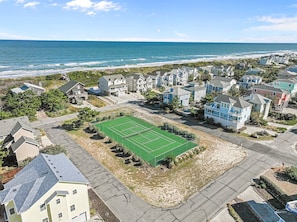 A residential area with houses, a tennis court, and a beach in the background.