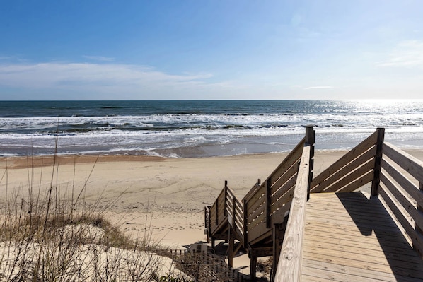 A wooden boardwalk leading to a beach with waves in the background.