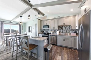A modern kitchen with stainless steel appliances, a large island, and a dining area with a view.