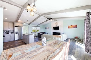 A modern kitchen with a central island, a dining area with a view, and a living space with a TV and artwork.