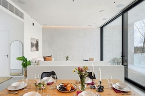 A modern dining area with a table set for two, a large window, and a minimalist interior design.