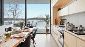 A modern kitchen with a large window, a dining area with a table set for two, and a view of a body of water. - Smart Home | Cinema | Sauna | Sonos Audio | Garage (Espoo)