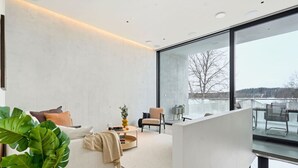 A modern living room with a sofa, coffee table, and chairs, a large window with a view of a snowy landscape, and a glass partition. - Smart Home | Cinema | Sauna | Sonos Audio | Garage (Espoo)