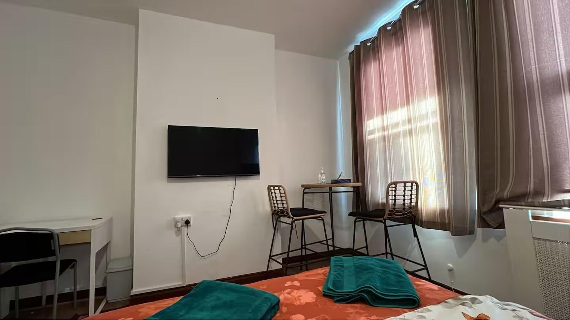 Une chambre d’hôtel avec un lit, deux chaises, un bureau, une télévision et une fenêtre avec des rideaux.