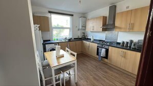 A compact kitchen with a dining table, a washing machine, a stove, and wooden cabinets. - House - Sleeps 10 - Honor Oak Park Station 2 Mins Walk (London)