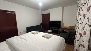 Quarto de hotel com cama, televisão, escrivaninha e cadeira.