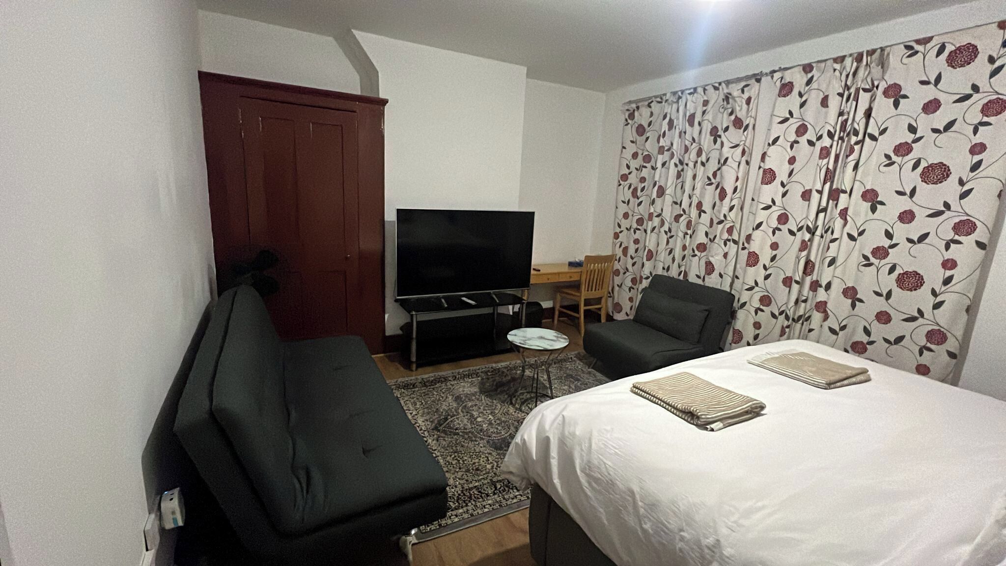 A hotel room with a bed, a TV, a desk, a chair, and a wardrobe.