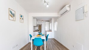 Eine moderne Küche mit weißen Schränken, einem Esstisch mit blauen Stühlen und einer sichtbaren Klimaanlage.