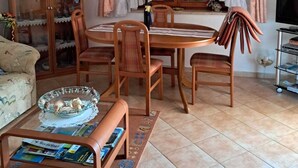 Een eetgedeelte met een houten tafel en stoelen, een kast met glazen deuren, een bank en een tv-meubel.