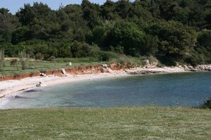 A coastal landscape with a clear beach, a rocky shoreline, and dense forest in the background. - Charming One-Bedroom apartment, Parking Included (Premantura)