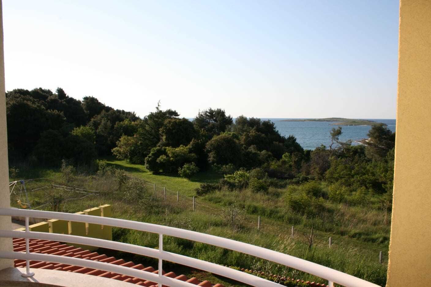 En balkon med udsigt over et kystlandskab, inklusive træer og et vandareal.