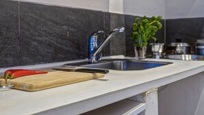 A kitchen with a modern design, featuring a stainless steel sink, a wooden cutting board, and a red pepper.
