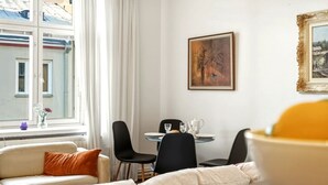 A modern room with a sofa, dining table, chairs, a painting, and a window with a view of buildings.