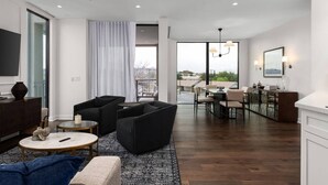Ein modernes Wohnzimmer mit Sofa, Sessel, Couchtisch und Essbereich mit Stühlen und Tisch.