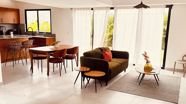 A modern living room with a sofa, chairs, a dining table, and a kitchen area. - Elegant 3-bedroom Villa in Harmony Village Vista Cana (Punta Cana)