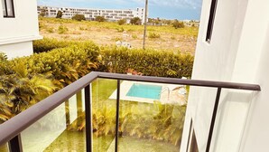 A balcony with a glass railing overlooking a swimming pool and a landscaped garden. - Elegant 3-bedroom Villa in Harmony Village Vista Cana (Punta Cana)