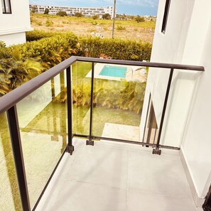 Ein Balkon mit Glasgeländer, der einen Pool und einen angelegten Garten blickt.