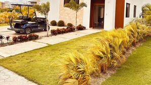 A modern two-story building with a flat roof, large windows, and a well-maintained lawn with tropical plants. - Elegant 3-bedroom Villa in Harmony Village Vista Cana (Punta Cana)