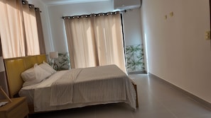 Ein Schlafzimmer mit Bett, Nachttisch, Lampe, Vorhängen und einer Wand-Klimaanlage.