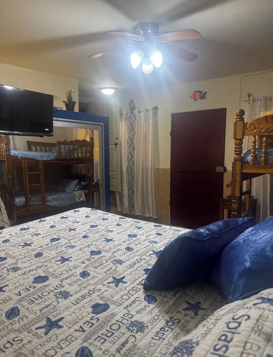 Een slaapkamer met een bed, een plafondventilator, een televisie, een houten stoel en een deur.