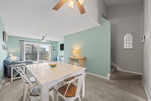 Ein Essbereich mit weißem Tisch und Stühlen, einem Deckenventilator und Blick ins Freie.