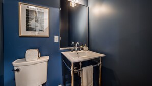 Un baño con inodoro y lavamanos blancos, un espejo y un cuadro en la pared.