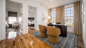 Habitación de hotel con piso de madera, un escritorio con lámpara, dos sillas, una cama y vistas al exterior.