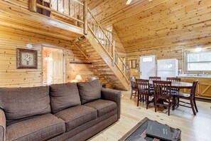 Ein Holzblockbau-Innenraum mit einer Couch, einem Esstisch, Stühlen und einer Treppe.