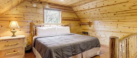 Een houten slaapkamer met een bed, een dressoir, een lamp en een raam.