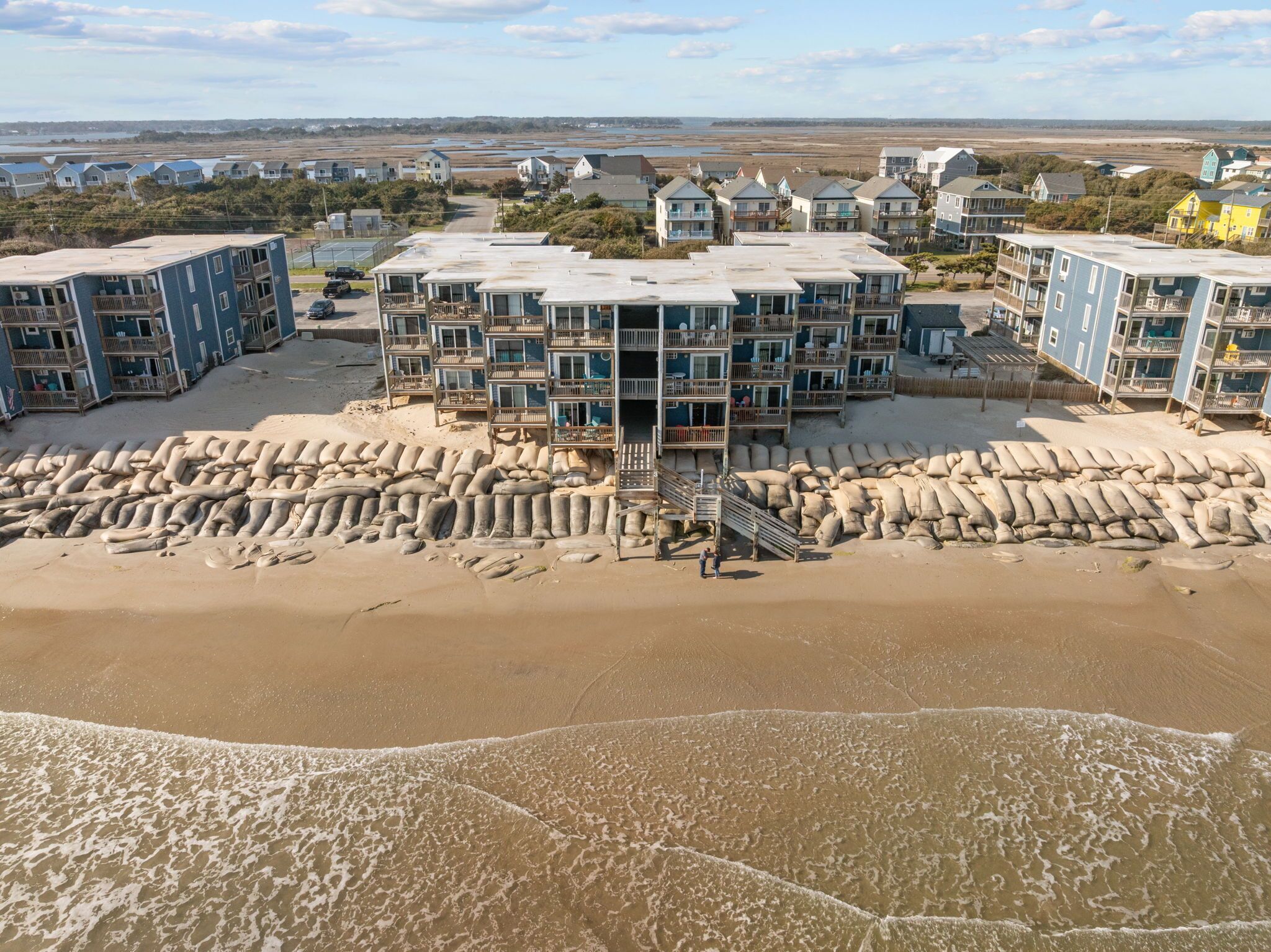 A beachfront hotel with multiple balconies, a sandy beach in front, and a view of the ocean.
